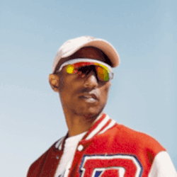 Pharrell Williams wearing speed dealer sunglasses and a cap, standing in the sun.